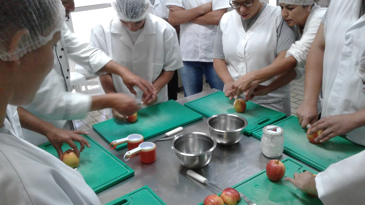Grupo de aprendizes com aventais de cozinha em torno de mesa com frutas e potes de vidros