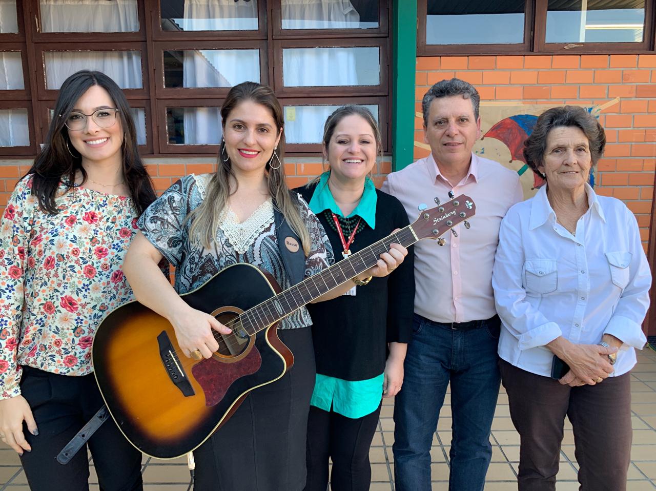 Juliana Buratto posa para foto com violão ao lado da coordenadora do CEVI, do presidente, da assistente Mariana Fritzen e da mãe Marileide Peixoto.