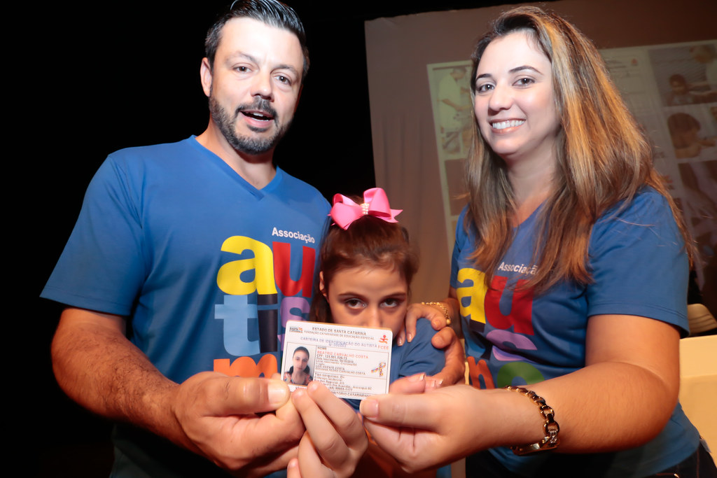 Um homem, uma mulher e uma menina posam para foto mostrando uma carteirinha
