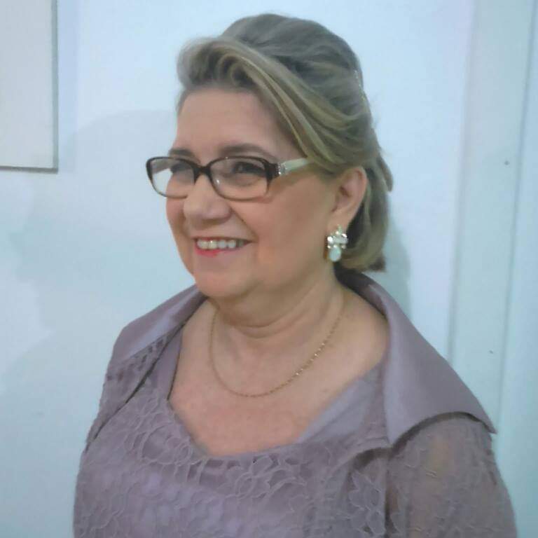 Retrato de mulher de meia idade, cabelos loiros e pelo ombro, óculos, sorrindo, vestido de festa