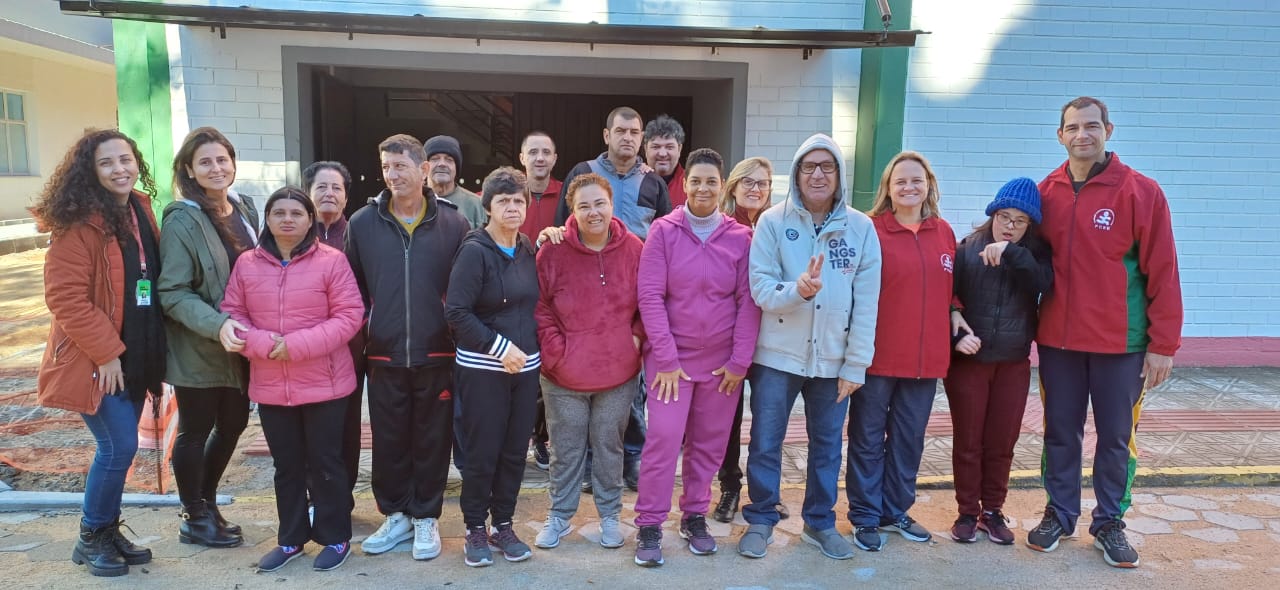 Um grupo de dezesseis pessoas em pé posam para uma foto em frente ao ginásio de esportes da Fundação Catarinense de Educação Especial