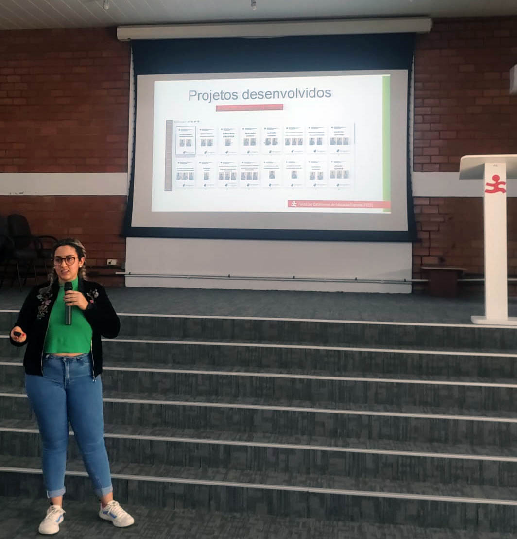 Mulher fala ao microfone a frente de palco