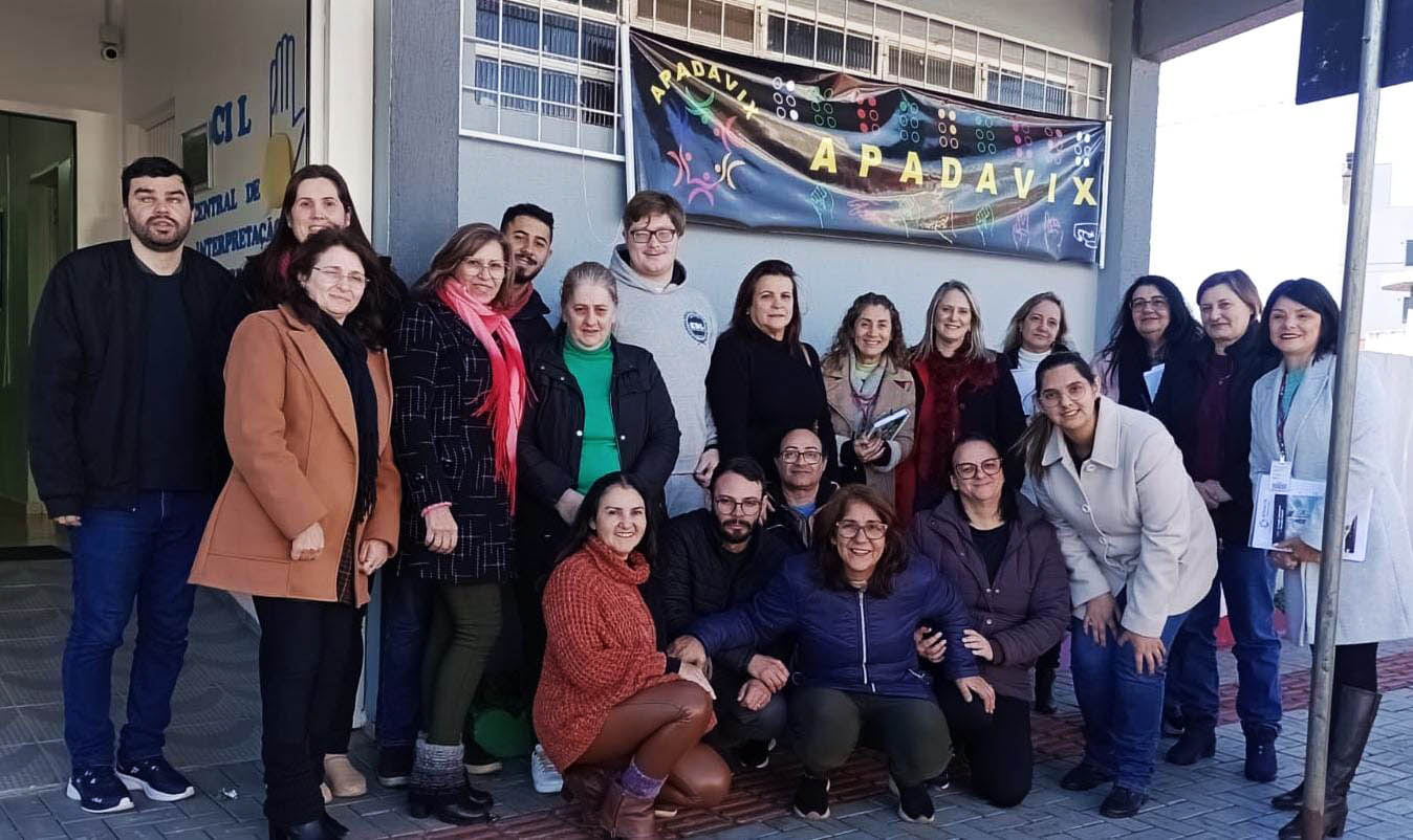 Quinze pessoas em pé posam para foto em ambiente externo