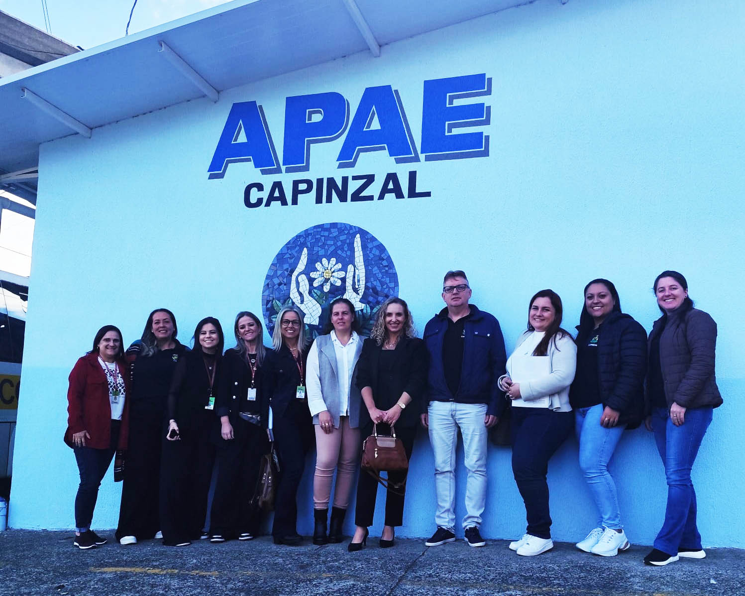 Apae de Capinzal recebe assessoria técnica fachada escrita apae capinzal e dez pessoas em pé posando para foto
