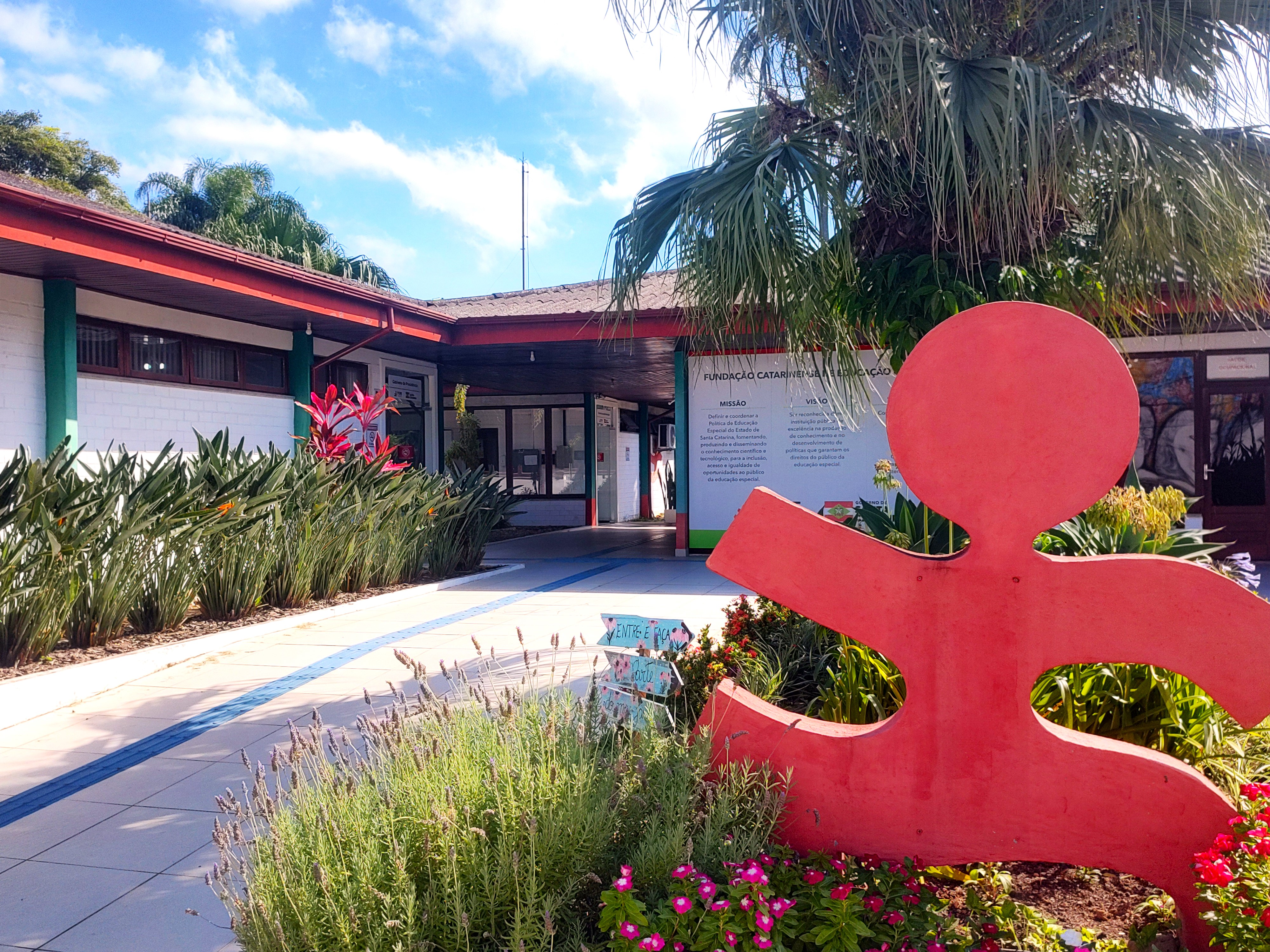 imagem da entrada da fcee, prédios térreos ao fundo, estátua do boneco vermelho a frente