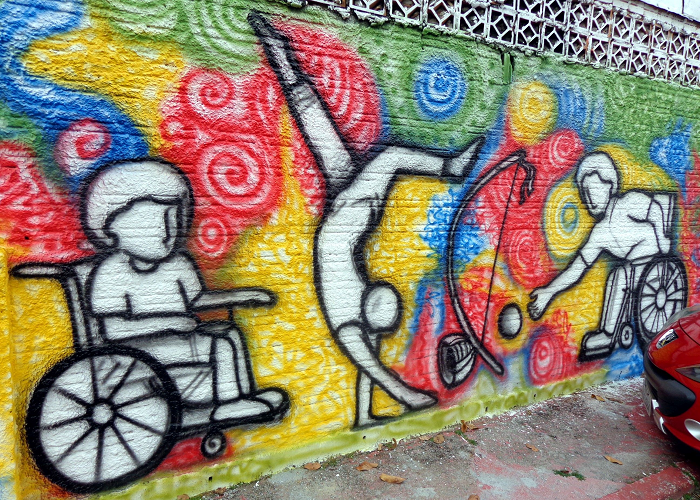 Pintura colorida em mural com desenho de dois cadeirantes jogando capoeira