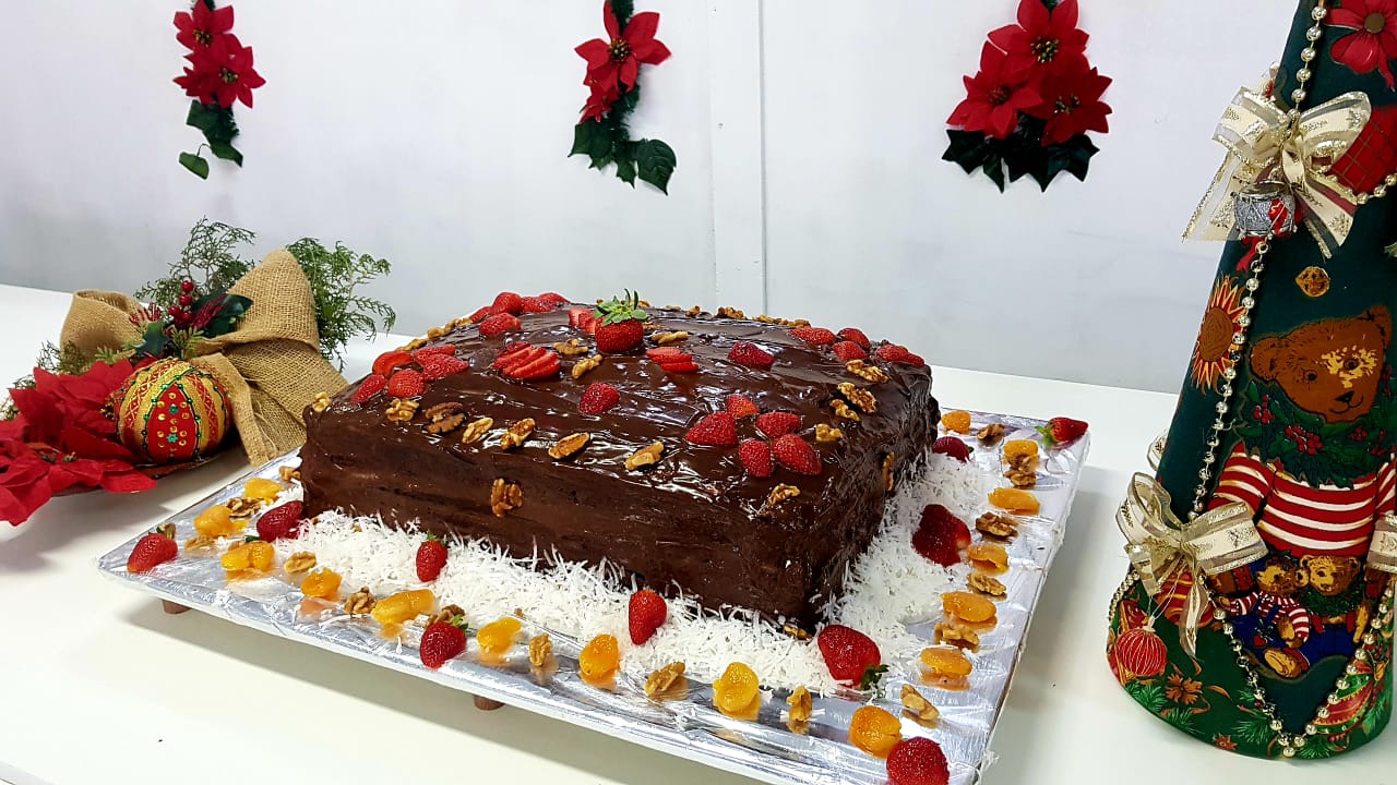 Imagem de bolo de chocolate retangular enfeitado com morangos e outros adornos de Natal